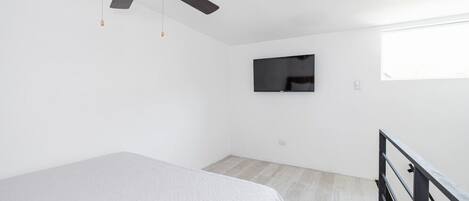 Une chambre à coucher avec un lit, un ventilateur de plafond, un téléviseur fixé au mur et une fenêtre.