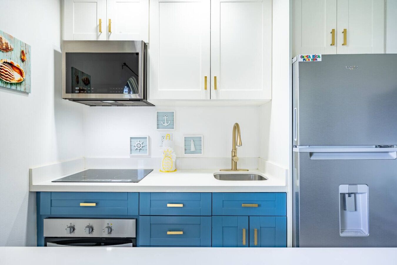 A modern kitchen with white cabinets, a stainless steel refrigerator, a microwave, and a sink with a gold faucet.
