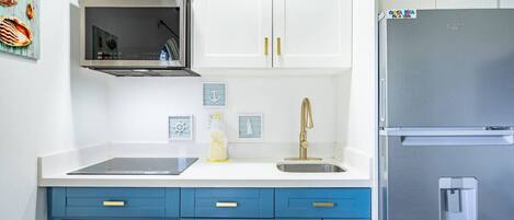 A modern kitchen with white cabinets, a stainless steel refrigerator, a microwave, and a sink with a gold faucet.