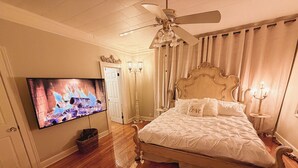 Quarto com cama grande, ventilador de teto, televisão exibindo uma lareira e um candelabro.
