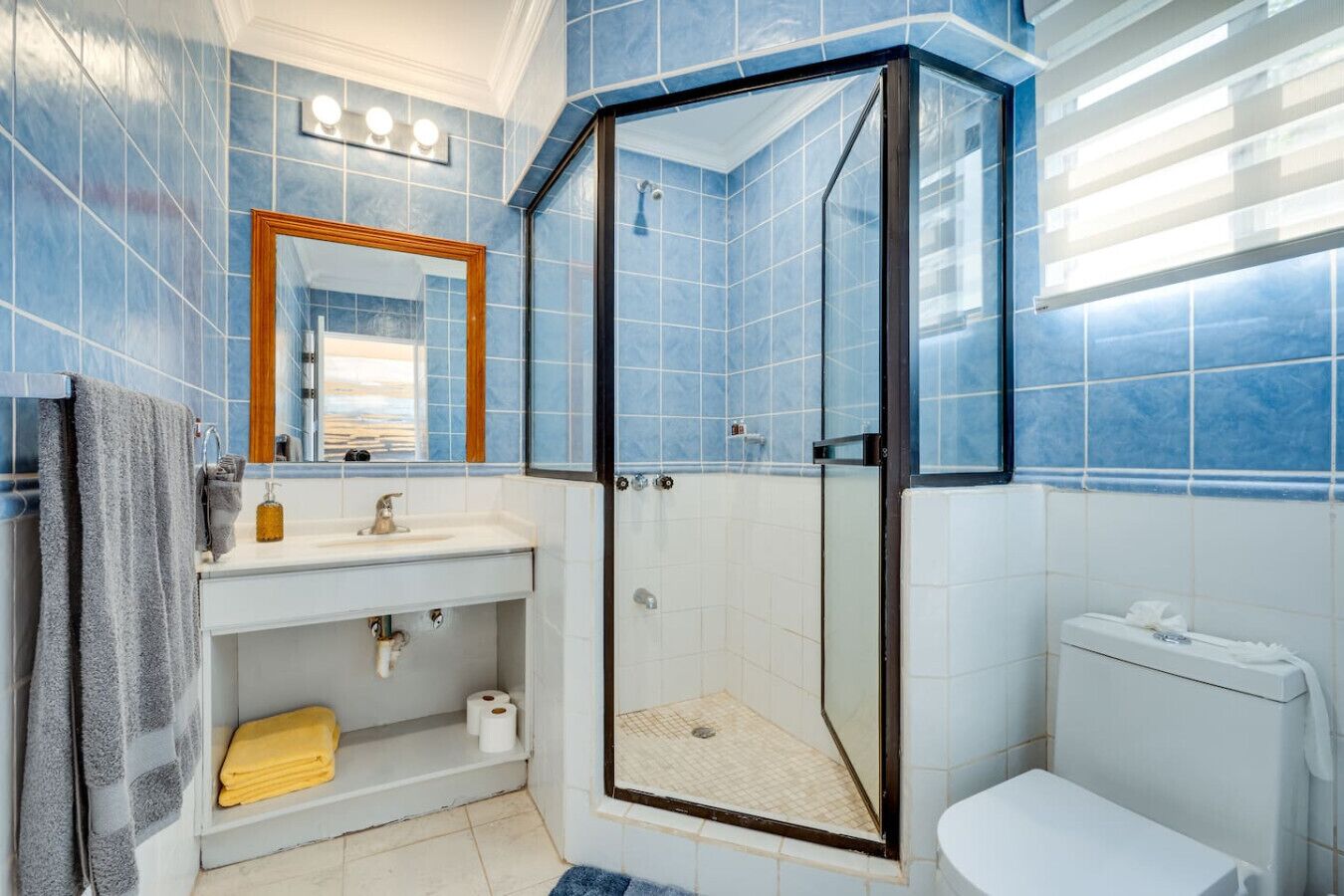 A bathroom with blue tiles, a glass-enclosed shower, a sink with a mirror, and a toilet.