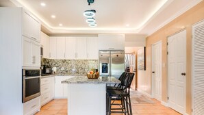 Una cocina moderna con armarios blancos, encimera de granito y una isla central con taburetes de bar.