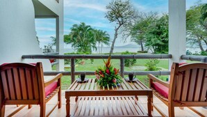 Una mesa de madera con dos sillas en un balcón con vistas a un jardín exuberante y una masa de agua.