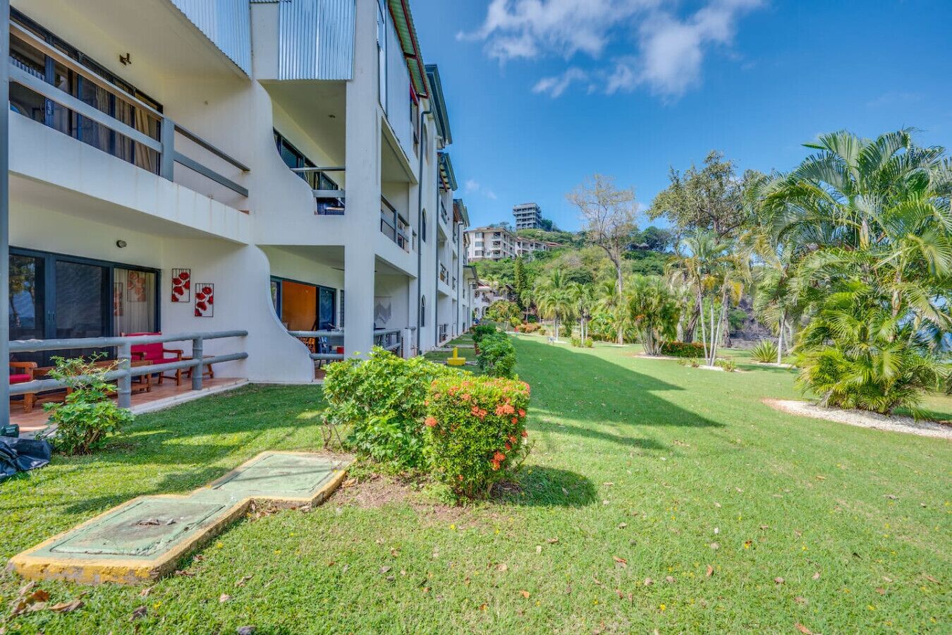 A modern hotel with a covered outdoor seating area, a well-maintained lawn, and a view of the surrounding landscape.
