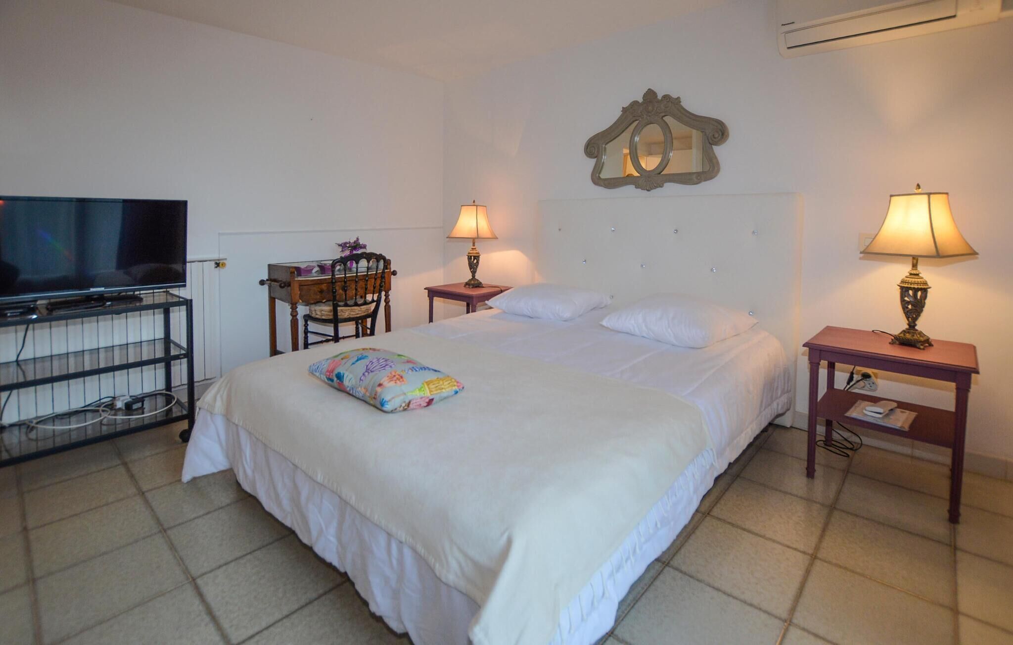 Una camera d'albergo con un letto, due comodini con lampade, una sedia, una televisione e uno specchio a parete.
