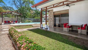 En moderne udendørs terrasse med swimmingpool, overdækket siddeområde og en stenvæg.