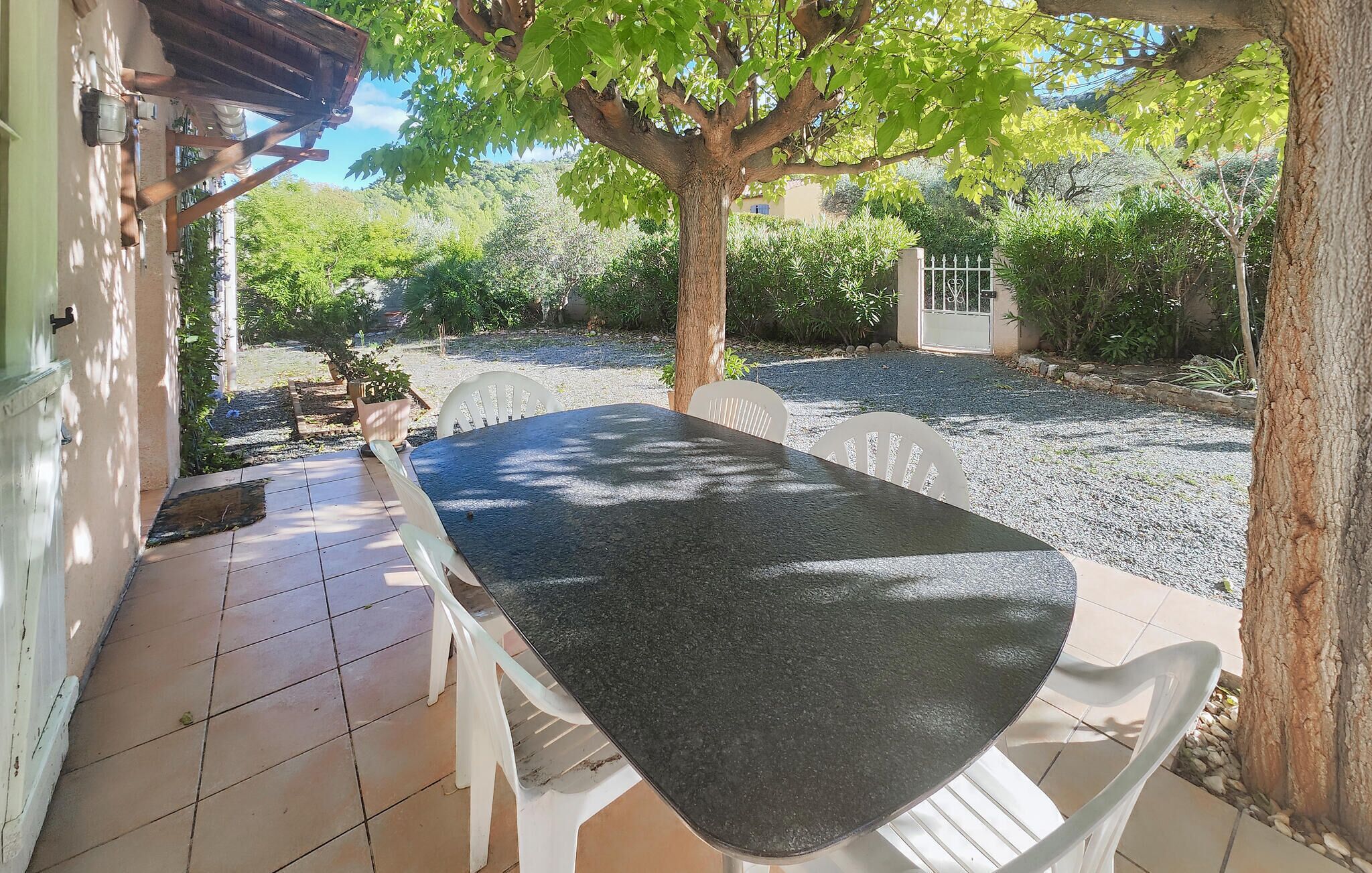 An outdoor patio with a table and chairs, surrounded by trees and a gravel path.