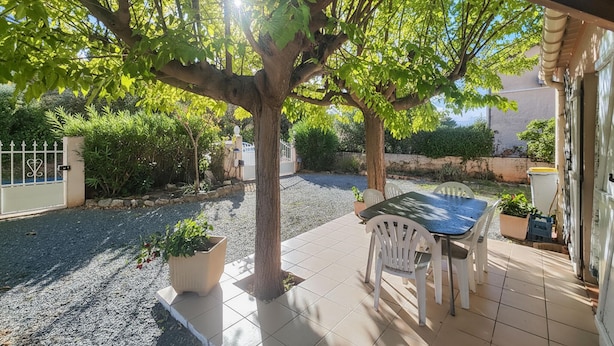 Un patio con tavolo e sedie, circondato da un'area ghiaiosa e un albero.