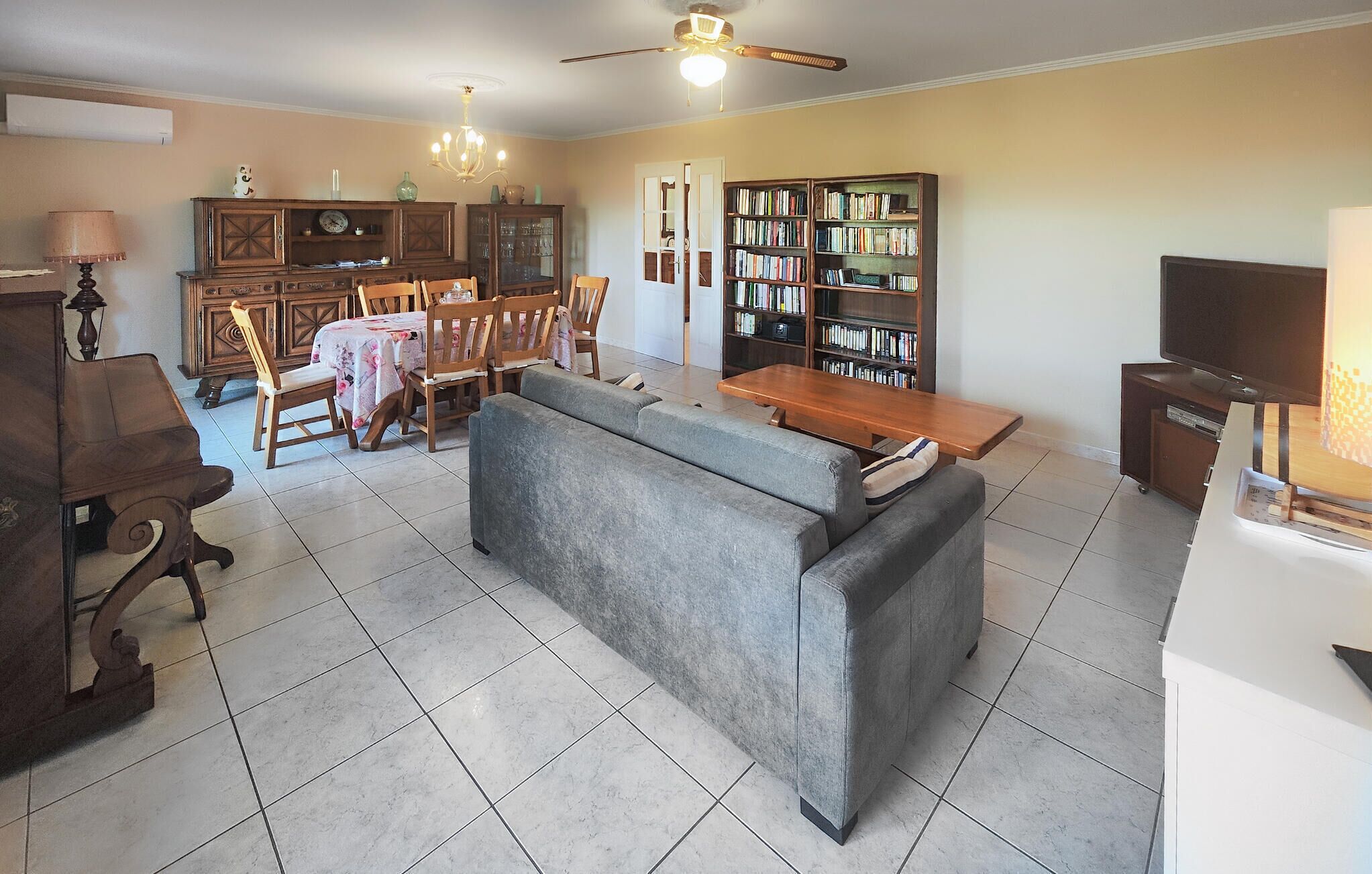 Una sala de estar con sofá, mesa de comedor, sillas, estantería y televisor.
