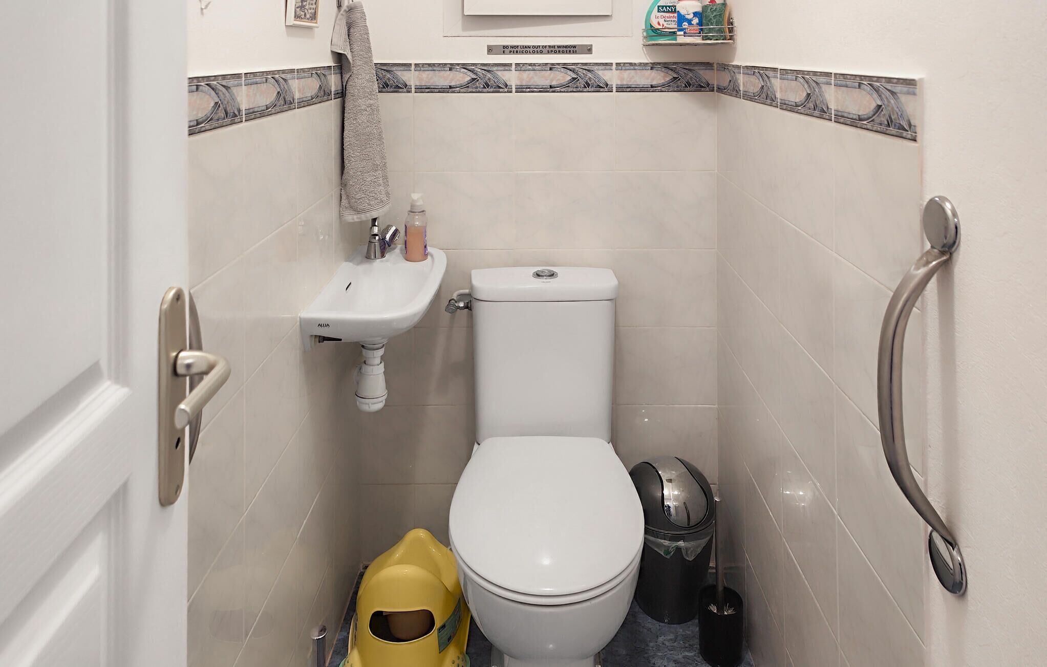 Ein kleines Badezimmer mit Toilette, Waschbecken und Haltegriffen.