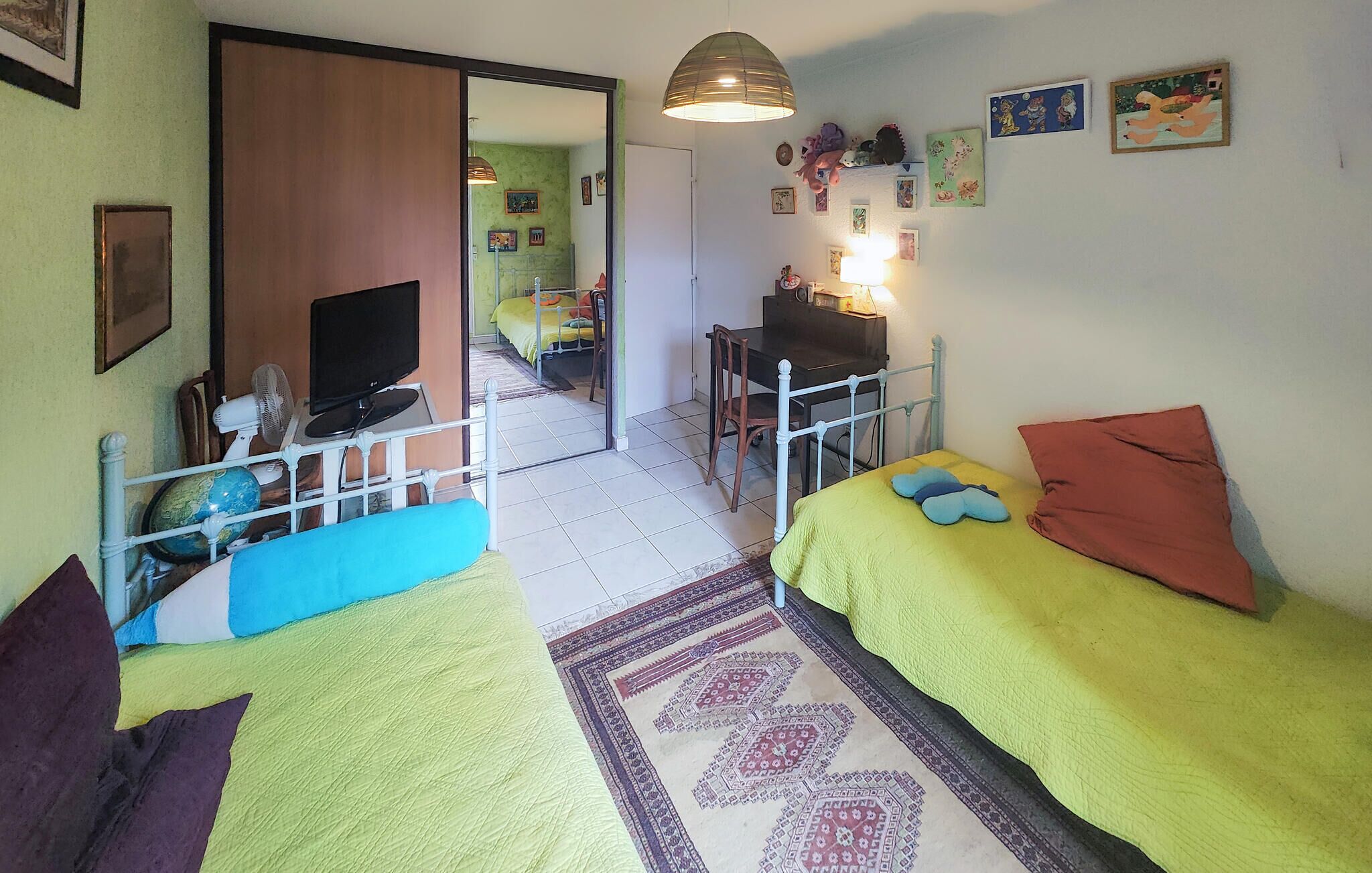 A small, cozy room with two single beds, a desk, a chair, a TV, and a globe.