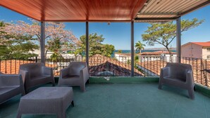 Un espace extérieur aménagé avec des meubles en osier, protégé par un auvent, offrant une vue sur la mer et adossé à un mur en pierre.