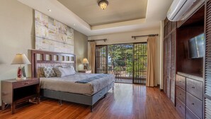 Une chambre à coucher avec un lit, un plancher en bois, une télévision et un balcon avec des rideaux.