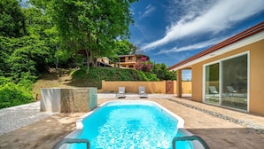 A swimming pool with clear blue water, surrounded by a patio area with lounge chairs and a building with large windows. - Serene Mar Azul Zen Villa w/ Pool & Yoga Platform (Huacas)