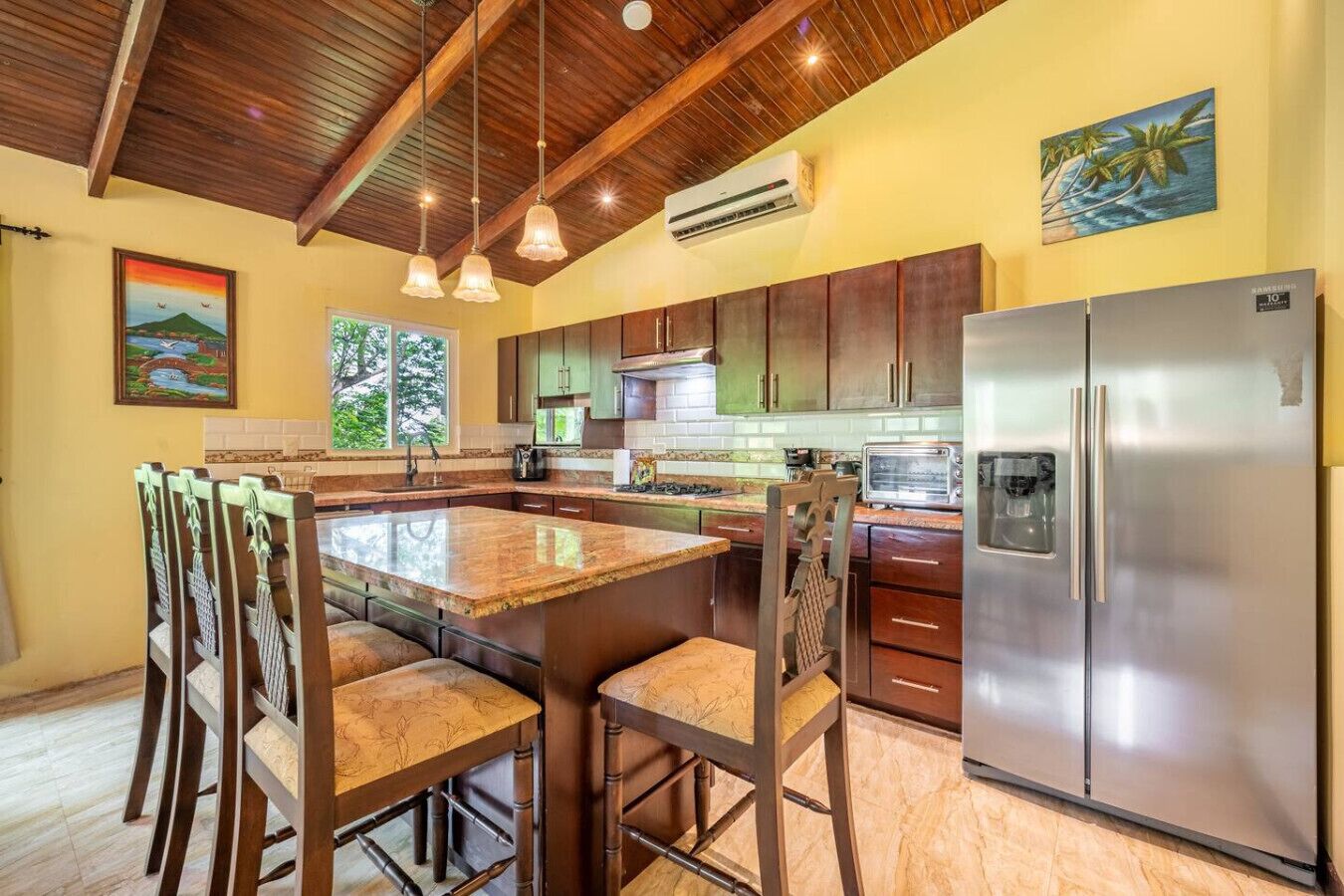 Una cocina con una isla central, sillas de madera, un refrigerador de acero inoxidable y un cuadro en la pared.