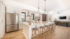 Cozinha moderna com uma ilha grande, eletrodomésticos de aço inoxidável e banquetas de madeira.