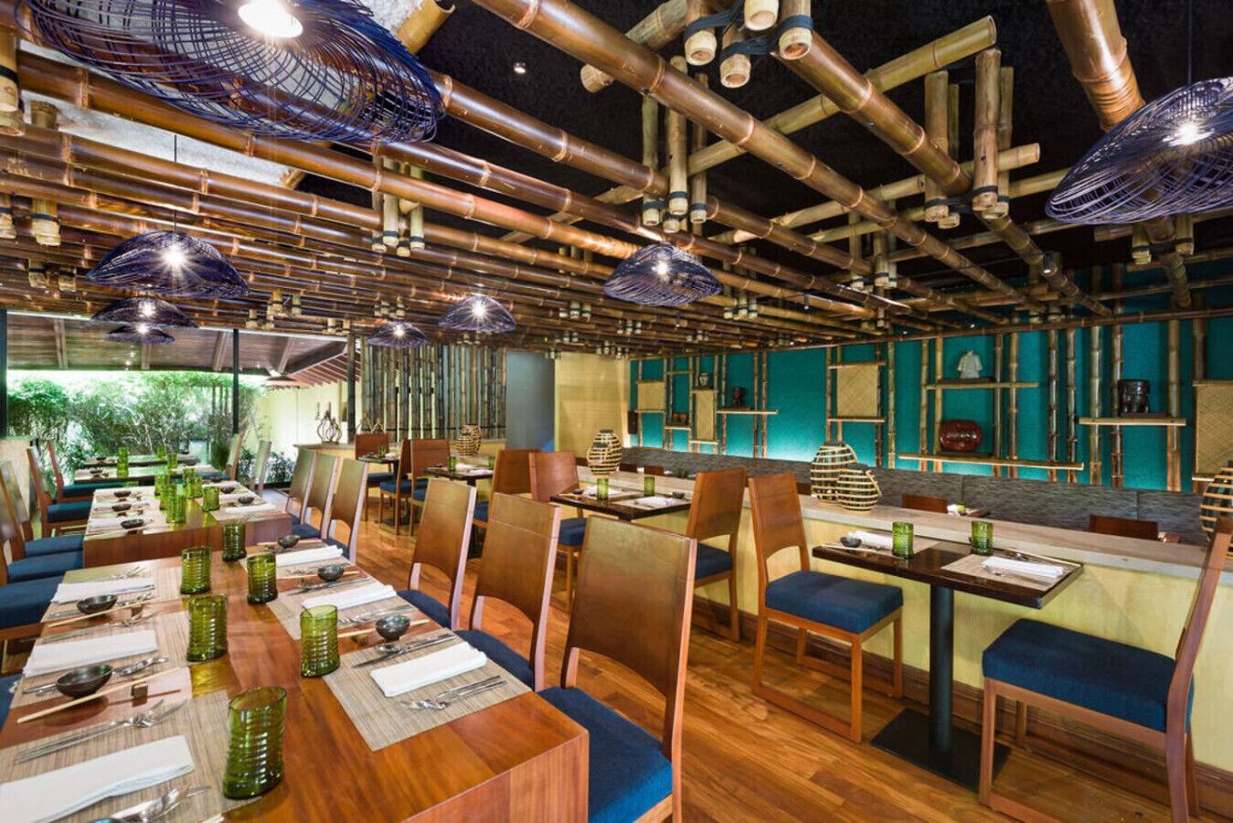A restaurant with bamboo ceiling structures, wooden tables, and blue cushioned chairs.