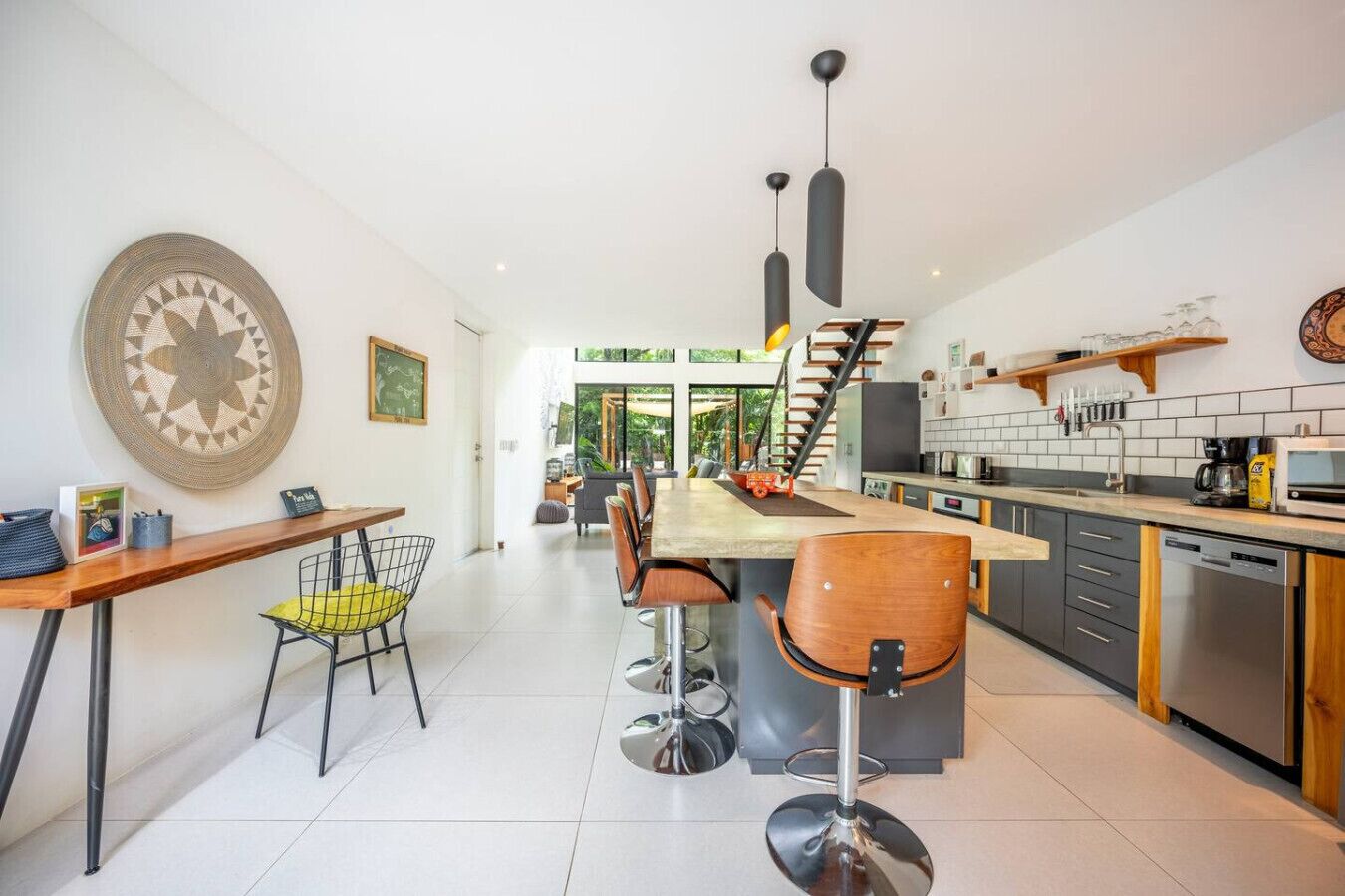Una cocina moderna con una isla central, taburetes de bar y una escalera que sube a un nivel superior.