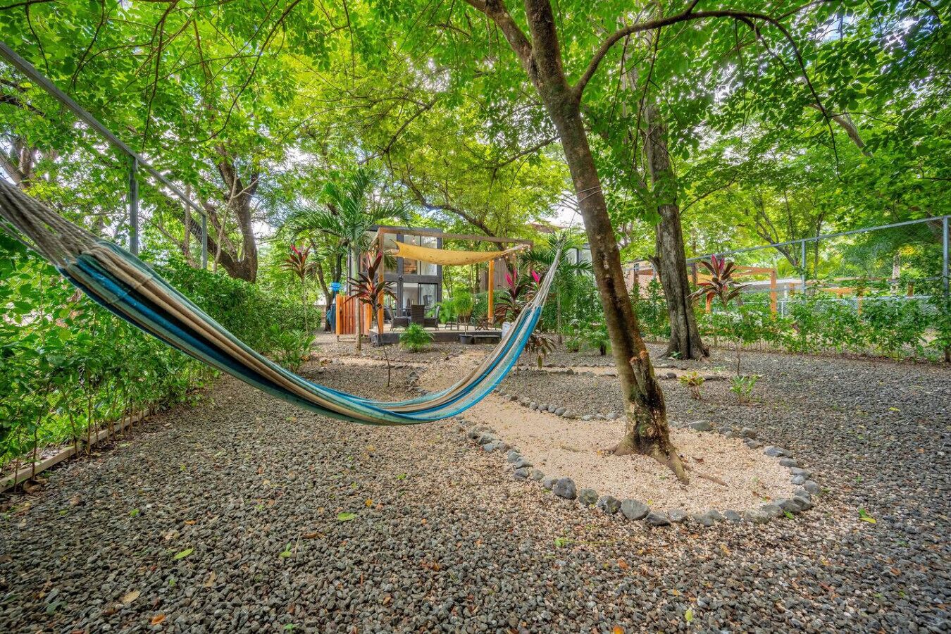 A hammock in a garden area with a seating area and a building in the background.