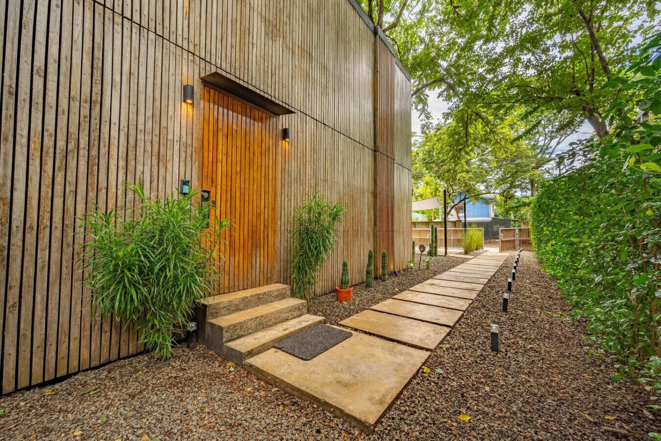A modern building with a wooden exterior, a wooden door, and a concrete pathway leading to the entrance.