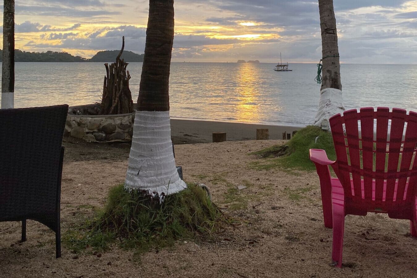 A beach view with a chair and a tree trunk.