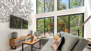A modern living room with a large window, a flat-screen TV, a wooden side table, and a grey sofa with decorative pillows. - Casa Teca in Surfside w/ Pool near Beach (Potrero)