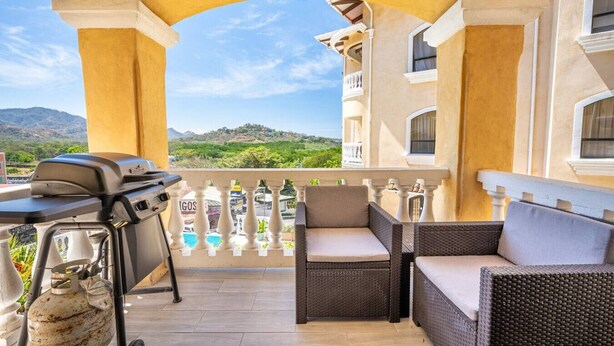 Eine Terrasse im Freien mit Korbmöbeln, einem Grill und Blick auf Pool und Berge.