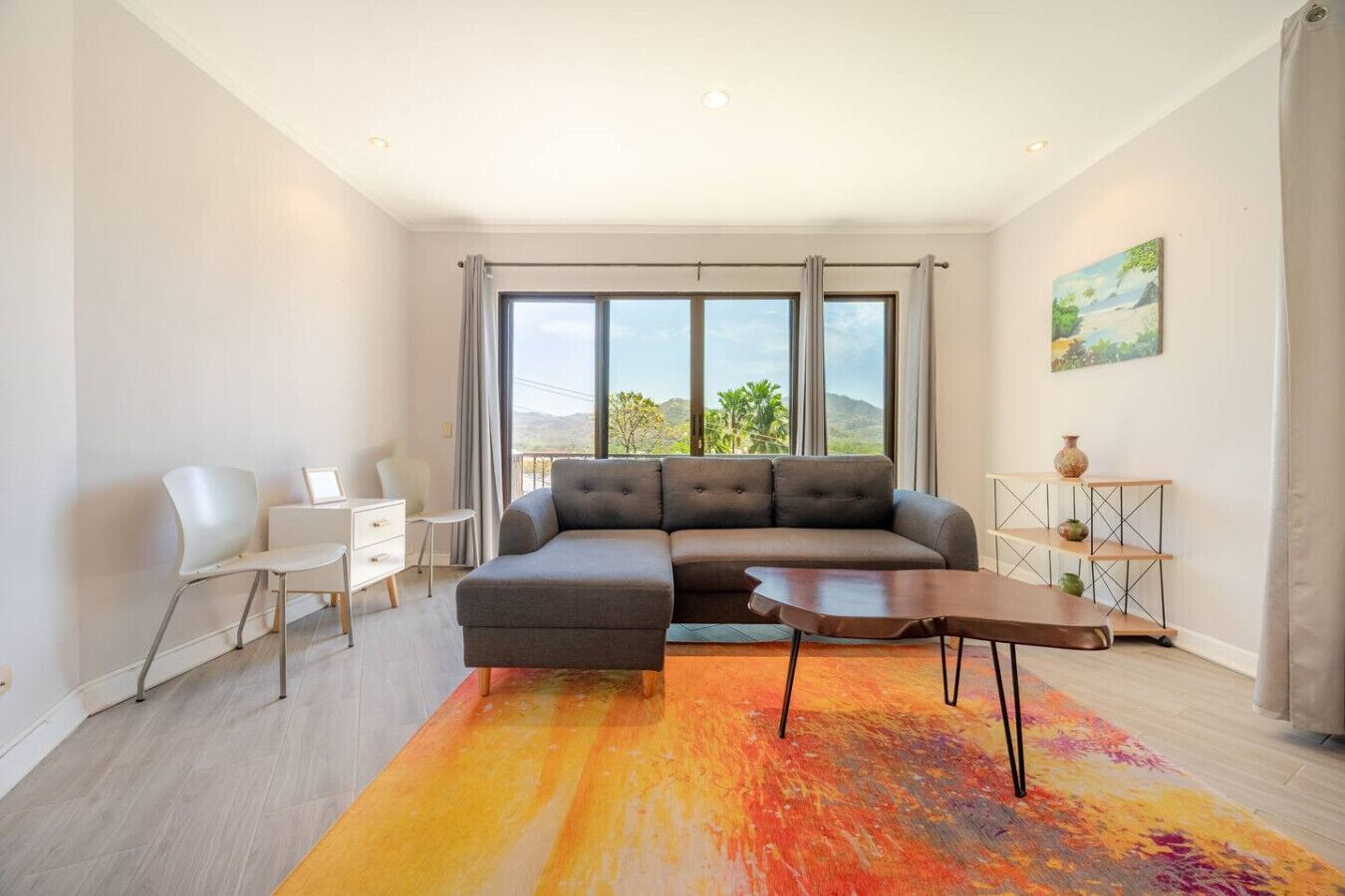 A modern living room with a sectional sofa, a small white desk, and a colorful rug.