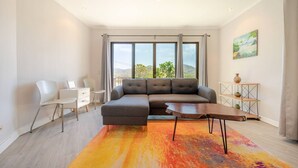 Ein modernes Wohnzimmer mit einem Ecksofa, einem kleinen weißen Schreibtisch und einem farbenfrohen Teppich.