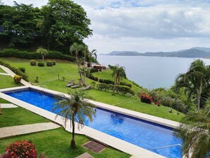 A rectangular swimming pool with a clear blue water, surrounded by well-maintained grass and palm trees. - Oceanfront Condo with Pool & Stunning Views (Playa Flamingo)