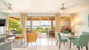 A spacious living area with a large glass door leading to a balcony with a view of a lake and mountains. There are ceiling fans, a dining table, and comfortable seating. - Oceanfront Condo with Pool & Stunning Views (Playa Flamingo)