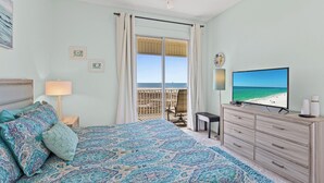 A bedroom with a bed, a TV, a dresser, and a balcony with a view of the beach. - The View ~ Top Floor ~ Amazing Views (Dauphin Island)