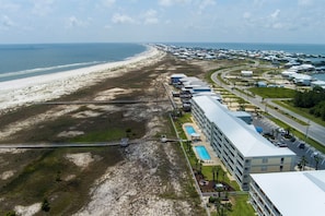 An aerial view of a coastal hotel with a beach, a swimming pool, and a parking area.