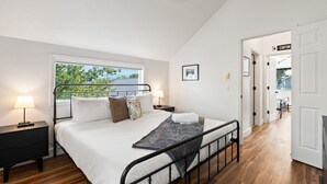 A bedroom with a bed, bedside tables, a window with a view, and a door leading to another room. - 2 Homes Downtown Whitefish w/ Hot Tubs & Big Yard (Whitefish)