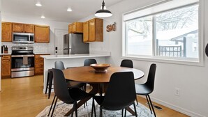A modern kitchen with wooden cabinets, stainless steel appliances, and a dining area with a round table and chairs. - 2 Homes Downtown Whitefish w/ Hot Tubs & Big Yard (Whitefish)