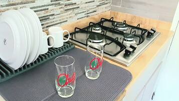Una cocina con estufa a gas, un escurreplatos con platos y tazas, y dos vasos sobre un tapete.