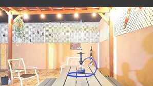 Un espacio al aire libre con mesa y sillas, un narguilé y una planta decorativa colgante.