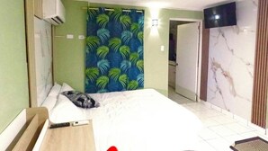 Una habitación de hotel con cama, aire acondicionado instalado en la pared, cortina con estampado de hojas, televisor y pared con diseño de mármol.