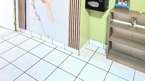 Una habitación con pared de mármol, un televisor instalado en la pared, un estante con un reloj y un juego de perchas de madera.