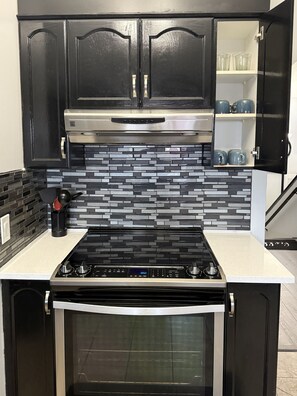 A kitchen with black cabinets, a stainless steel range hood, a black stove, and a tiled backsplash. - 9 min airport|Great view|Game room|Sleep 10|Garage (Calgary)