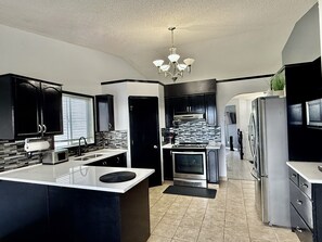 A modern kitchen with black cabinets, a stainless steel refrigerator, and a central island. - 9 min airport|Great view|Game room|Sleep 10|Garage (Calgary)