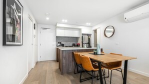 Una cocina moderna con armarios blancos, horno empotrado y cafetera. Hay una mesa de comedor con dos sillas y un espejo en la pared.