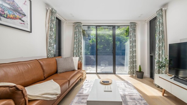 Una sala de estar moderna con un sofá de cuero marrón, una mesa de centro y un televisor sobre un mueble.