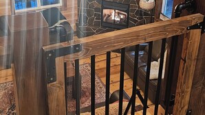 Ein Holzinnenraum mit Kamin aus Stein, einer Pendelleuchte und Blick ins Freie durch Fenster.