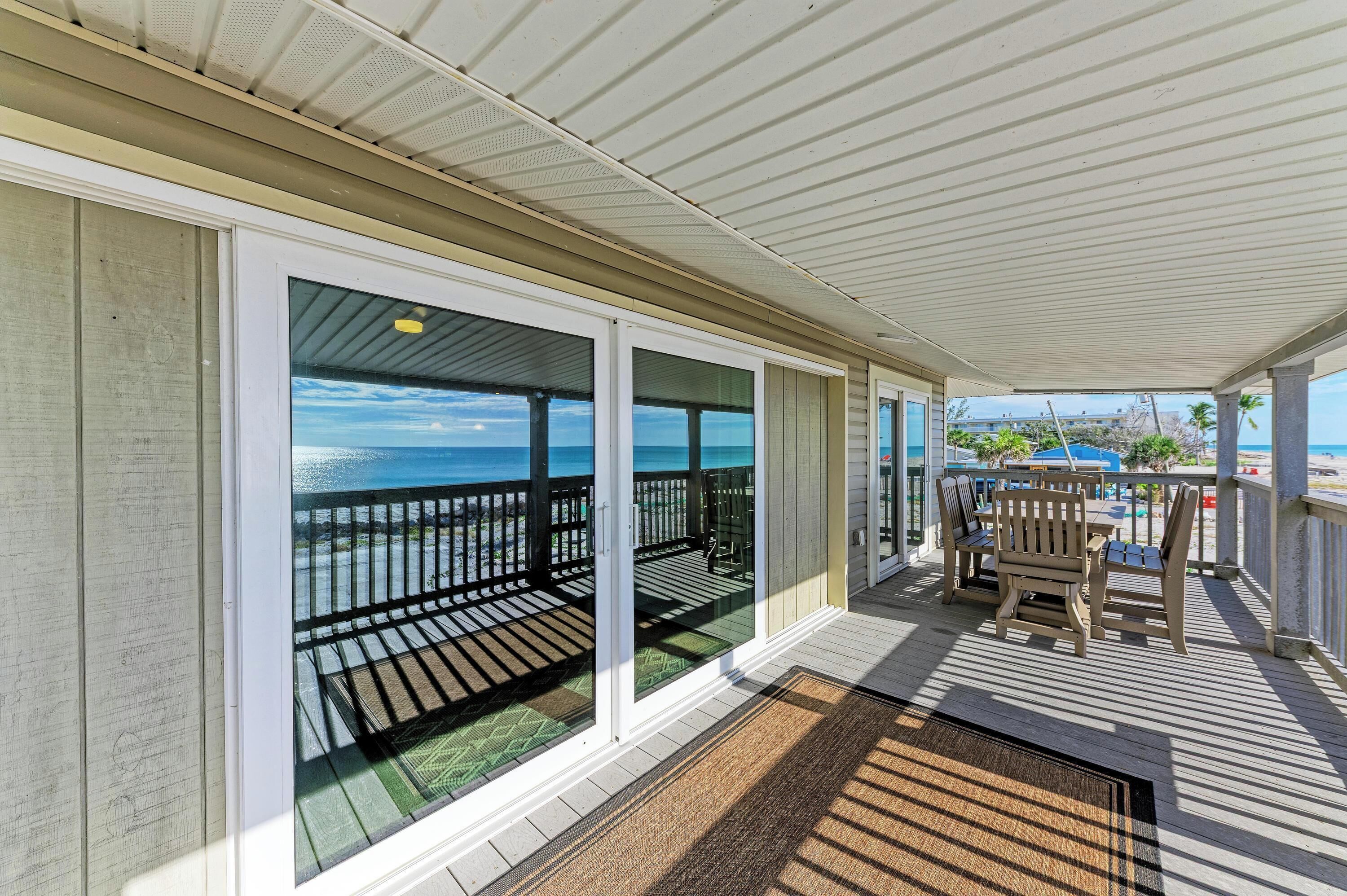 A covered outdoor deck with a view of the ocean, wooden chairs, and a table.