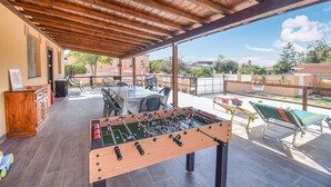 Een terras buiten met een tafelvoetbaltafel, een zithoek en uitzicht op de omgeving.