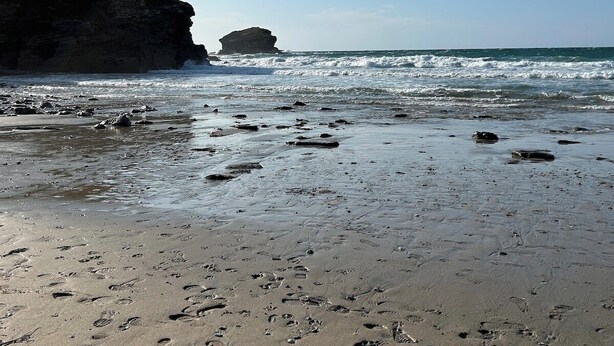 A beach with footprints in the sand, a rocky cliff, and the ocean.