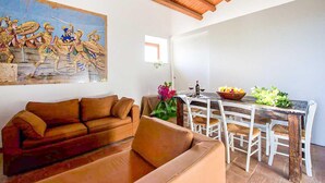 Uma sala de estar com um sofá marrom, uma mesa de jantar com cadeiras, um quadro na parede e teto de madeira.