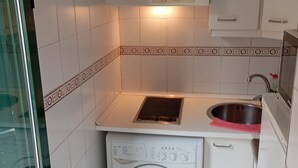 Pieni, käytännöllinen keittiö, jossa on pyykinpesukone, pesuallas ja kaappeja.
