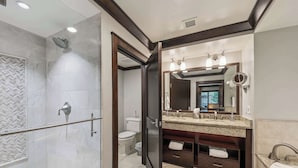 Un baño moderno con ducha envuelta en vidrio, tocador con un espejo grande y un inodoro.